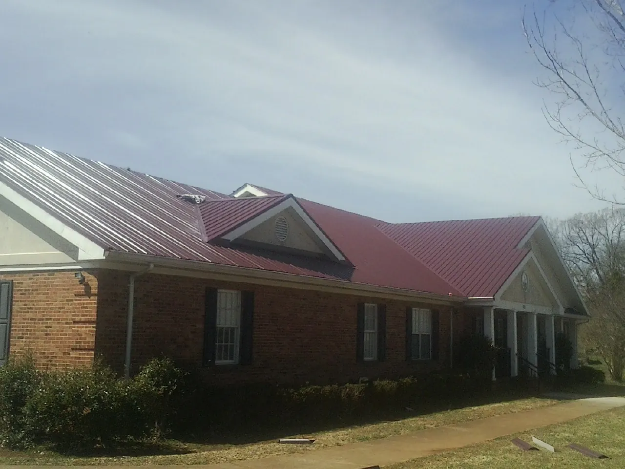 Red metal roof with gabled entries on a long brick building, from a Hail Damage Roof Repair job in Patuxent River