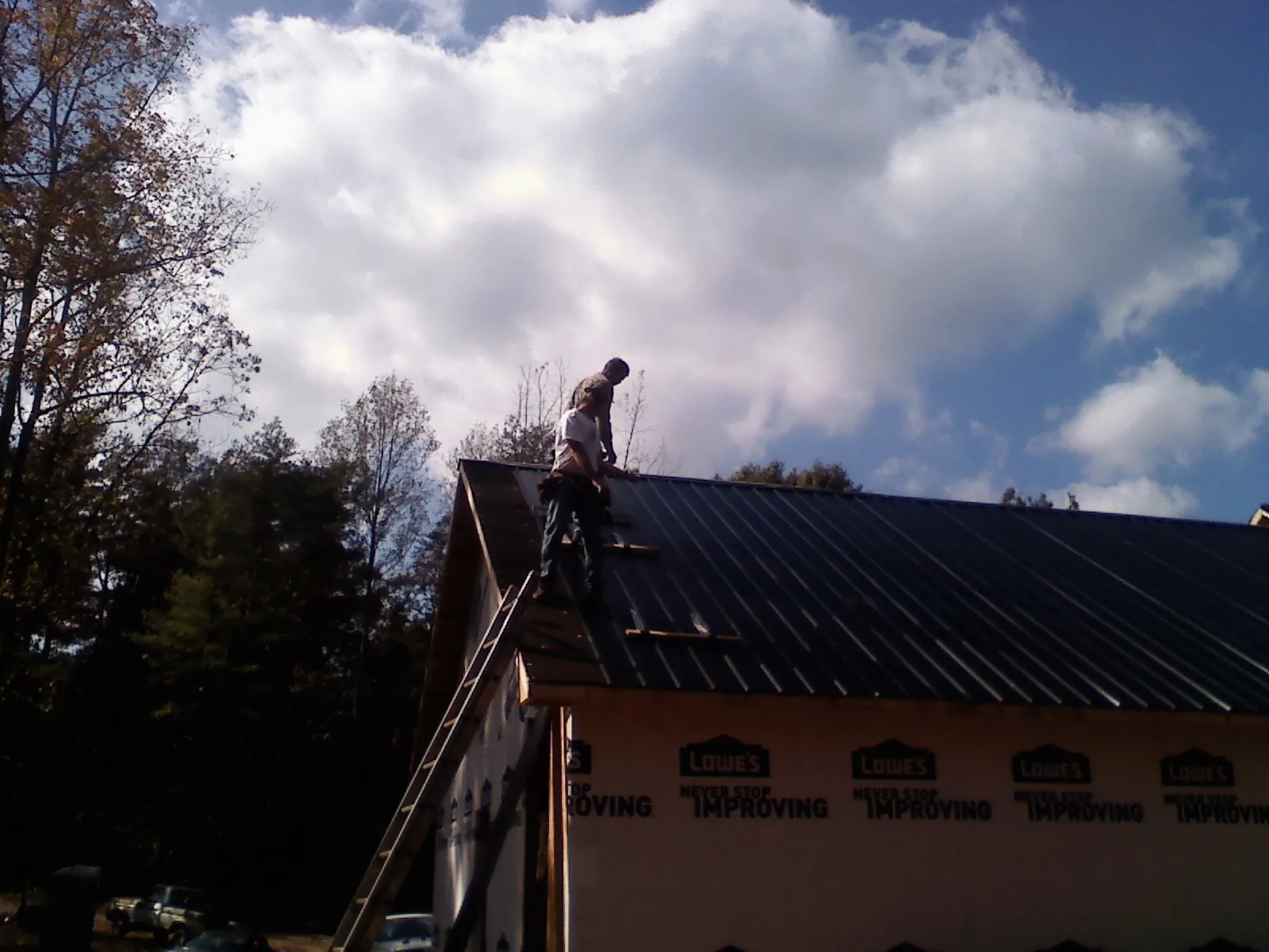 Roofer fastening dark metal panels high against a cloudy sky, from a Roof Inspection job in Patuxent River
