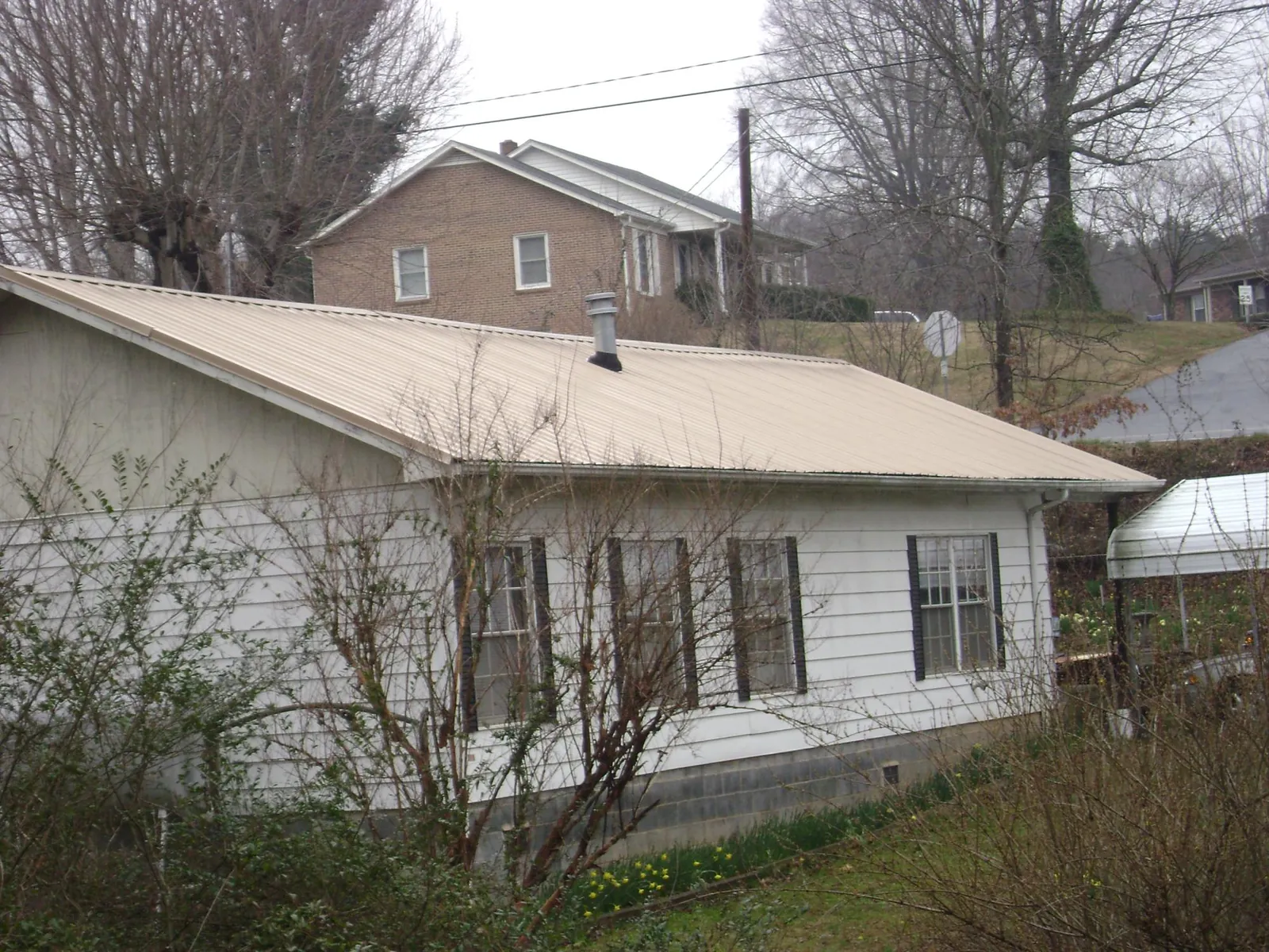 Tan metal roof on a white sided house set into a hillside — Commercial Roofing by Roofing Brothers in Patuxent River